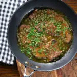 Overhead veal scallopini with lemon and capers in its cooking pan.