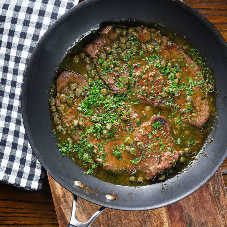 Overhead veal scallopini with lemon and capers in its cooking pan.