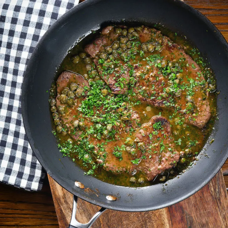 Overhead veal scallopini with lemon and capers in its cooking pan.