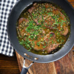 Overhead veal scallopini with lemon and capers in its cooking pan.