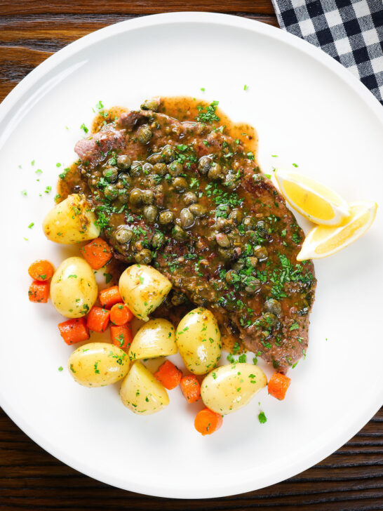 Overhead rose veal scallopini with lemon and capers (piccata) served with buttered potatoes and carrots.