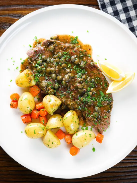 Overhead rose veal scallopini with lemon and capers (piccata) served with buttered potatoes and carrots.