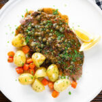 Overhead rose veal scallopini with lemon and capers (piccata) served with buttered potatoes and carrots.