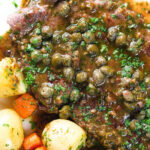 Overhead close-up veal scallopini with lemon and capers served with buttered potatoes and carrots.