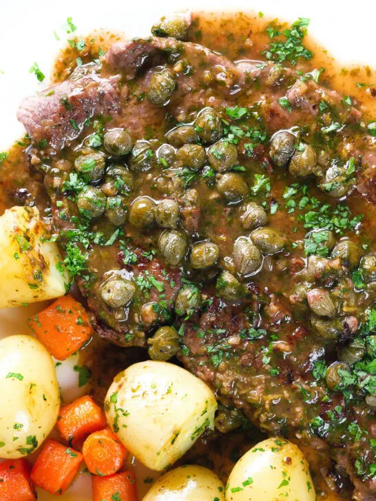 Overhead close-up veal scallopini with lemon and capers served with buttered potatoes and carrots.