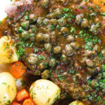 Overhead close-up veal scallopini with lemon and capers served with buttered potatoes and carrots.