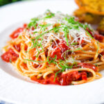 Spaghetti Napolitana or pasta pomodoro (tomato) garnished with basil and pecorino cheese.