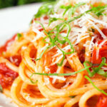 Close-up spaghetti Napolitana (Tomato Pasta) garnished with basil and pecorino cheese.