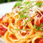 Close-up spaghetti Napolitana (Tomato Pasta) garnished with basil and pecorino cheese.