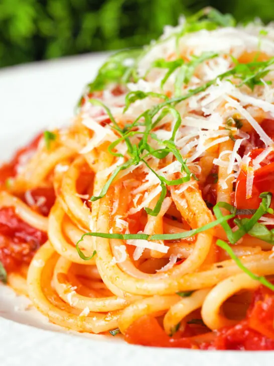 Close-up spaghetti Napolitana (Tomato Pasta) garnished with basil and pecorino cheese.
