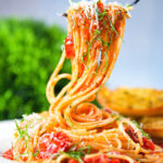 Spaghetti Napolitana (Pasta Pomodoro) garnished with basil and pecorino on a fork.