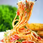 Spaghetti Napolitana (Pasta Pomodoro) garnished with basil and pecorino on a fork.