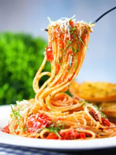 Spaghetti Napolitana (Pasta Pomodoro) garnished with basil and pecorino on a fork.