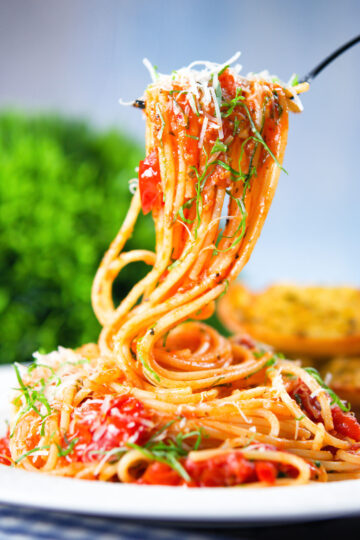 Spaghetti Napolitana (Pasta Pomodoro) garnished with basil and pecorino on a fork.