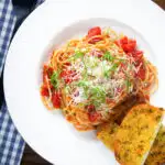 Overhead spaghetti Napolitana (Tomato Pasta) garnished with basil and pecorino cheese served with garlic bread.