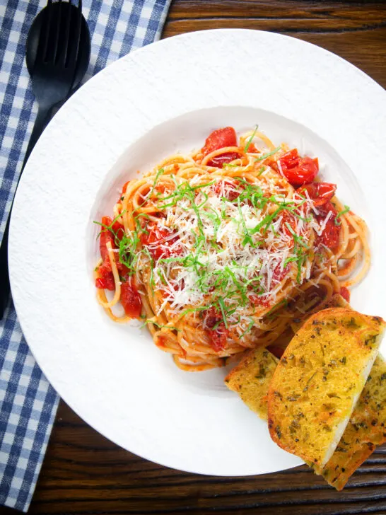 Overhead spaghetti Napolitana (Tomato Pasta) garnished with basil and pecorino cheese served with garlic bread.