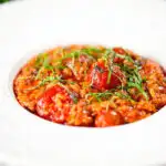 Spicy nduja sausage and cherry tomato risotto garnished with basil.