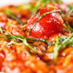 Close-up spicy nduja and cherry tomato risotto garnished with basil.