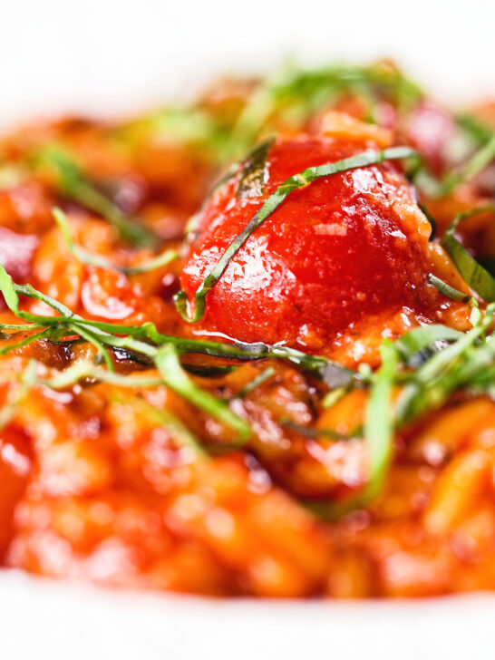 Close-up spicy nduja and cherry tomato risotto garnished with basil.
