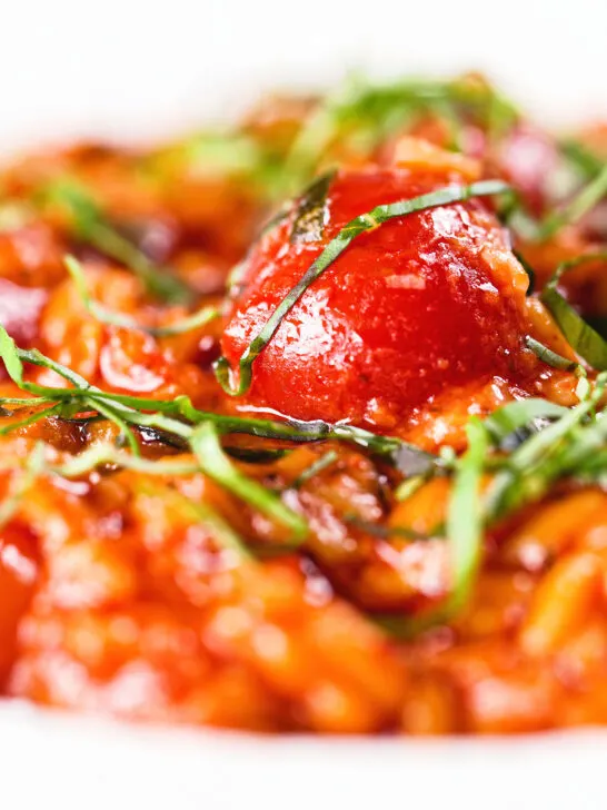 Close-up spicy nduja and cherry tomato risotto garnished with basil.