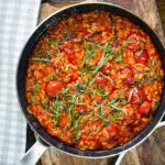 Overhead spicy nduja and cherry tomato risotto in a cooking pan.