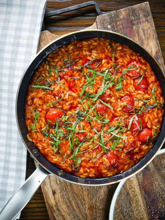 Overhead spicy nduja and cherry tomato risotto in a cooking pan.