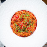 Overhead spicy nduja and cherry tomato risotto garnished with basil.