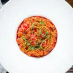 Overhead spicy nduja and cherry tomato risotto garnished with basil.