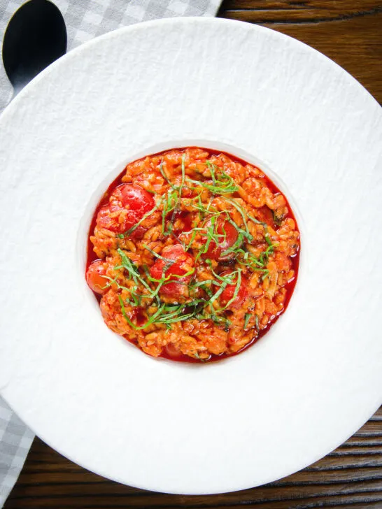 Overhead spicy nduja and cherry tomato risotto garnished with basil.