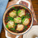 Overhead red wine and port venison stew or casserole with suet dumplings in a Dutch oven.