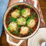Overhead red wine and port venison stew or casserole with suet dumplings in a Dutch oven.
