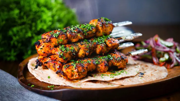 Chicken tikka kebab skewers garnished with coriander, served with chapati flatbreads.