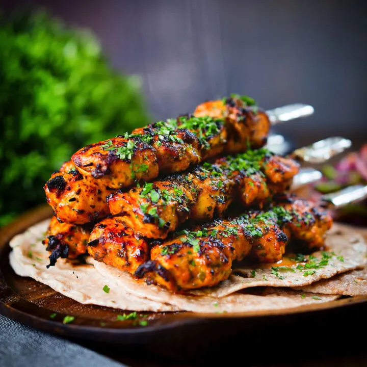 Chicken tikka kebab skewers garnished with coriander, served with chapati flatbreads.