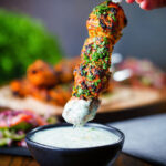 Chicken tikka kebab skewer being dipped into a mint and yoghurt raita style sauce.