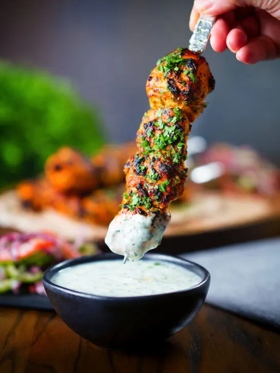 Chicken tikka kebab skewer being dipped into a mint and yoghurt raita style sauce.