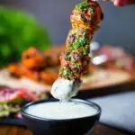 Chicken tikka kebab skewer being dipped into a mint and yoghurt raita style sauce.