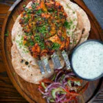 Overhead chicken tikka kebab skewers served with chapati, raita and kachumber salad.