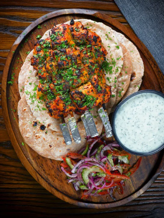 Overhead chicken tikka kebab skewers served with chapati, raita and kachumber salad.
