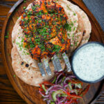 Overhead chicken tikka kebab skewers served with chapati, raita and kachumber salad.