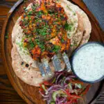 Overhead chicken tikka kebab skewers served with chapati, raita and kachumber salad.