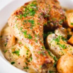 Close-up Somerset chicken legs in a creamy cider and cheddar sauce served with mini roast potatoes.
