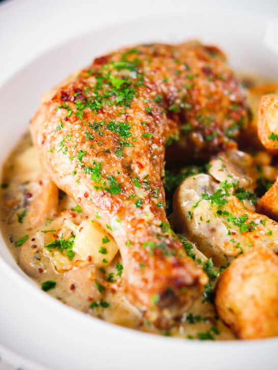Close-up Somerset chicken legs in a creamy cider and cheddar sauce served with mini roast potatoes.