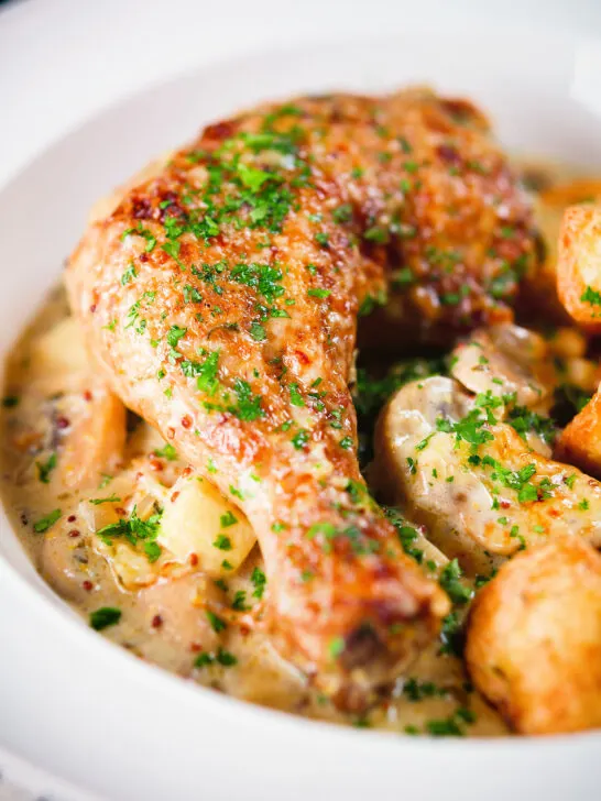 Close-up Somerset chicken legs in a creamy cider and cheddar sauce served with mini roast potatoes.