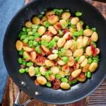 Pan fried gnocchi with crispy bacon, broad beans and parmesan cheese in a pan.