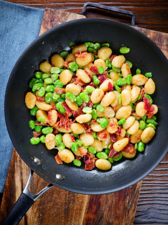 Pan fried gnocchi with crispy bacon, broad beans and parmesan cheese in a pan.