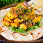 Persian joojeh kabob (saffron chicken skewers) served with flatbread, rocket and lemon wedges.