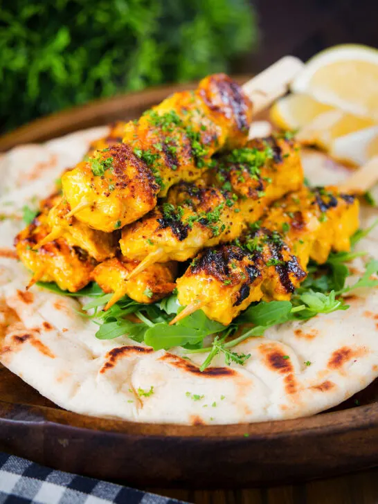 Persian joojeh kabob (saffron chicken skewers) served with flatbread, rocket and lemon wedges.