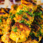 Close-up Persian joojeh kabob (saffron chicken skewers) garnished with parsley and sumac.