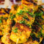 Close-up Persian joojeh kabob (saffron chicken skewers) garnished with parsley and sumac.