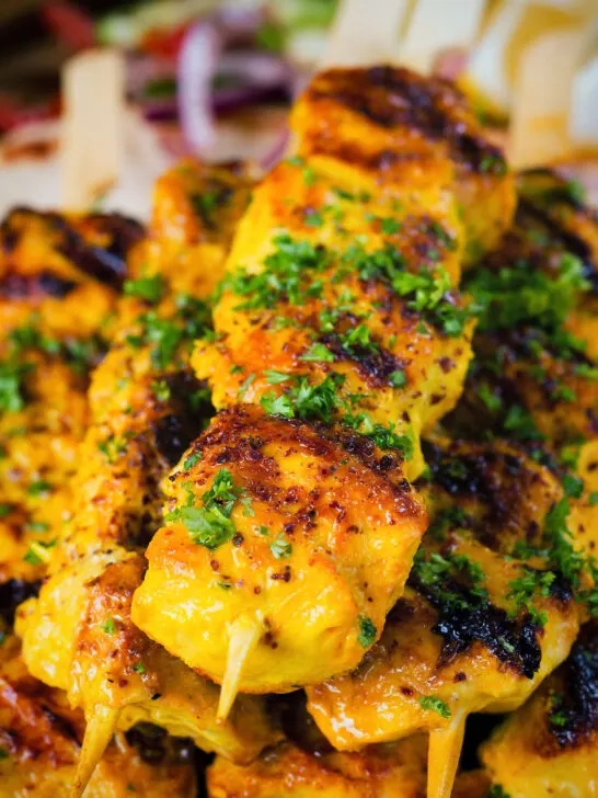 Close-up Persian joojeh kabob (saffron chicken skewers) garnished with parsley and sumac.